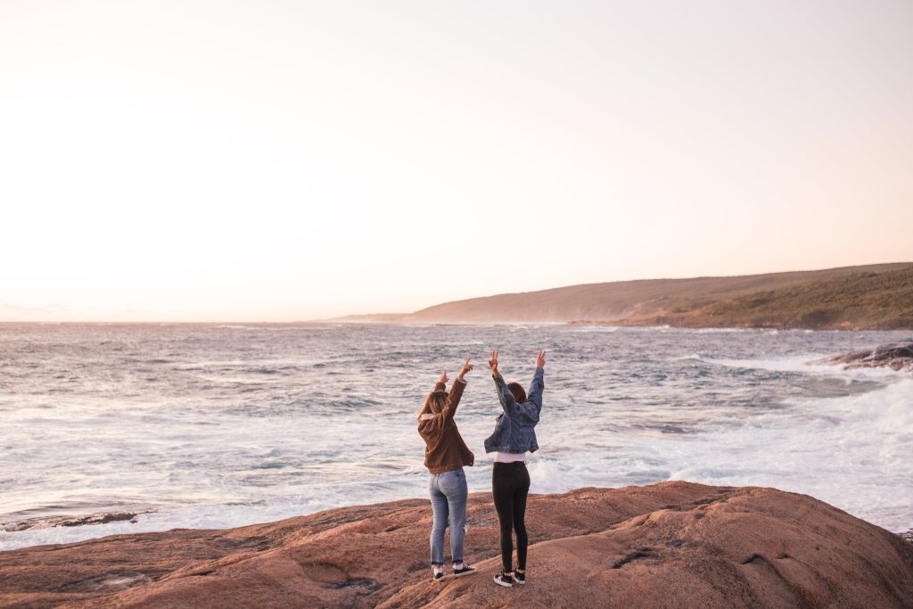 two women hands in the air at beach